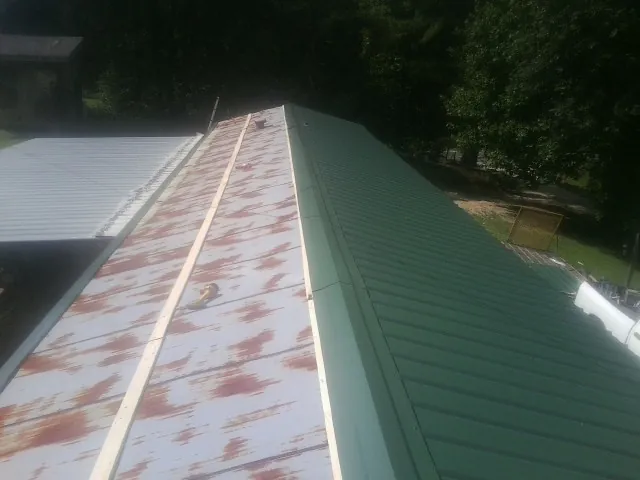 Old rusted panels beside newly installed green metal roofing — Wind Damage Roof Repair by Roofing Brothers in Wallops Island