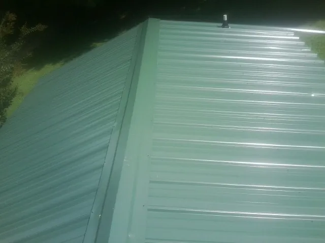 New green metal panels meeting at the ridge of a roof — Flat Roof Repair work by our crew in Wallops Island