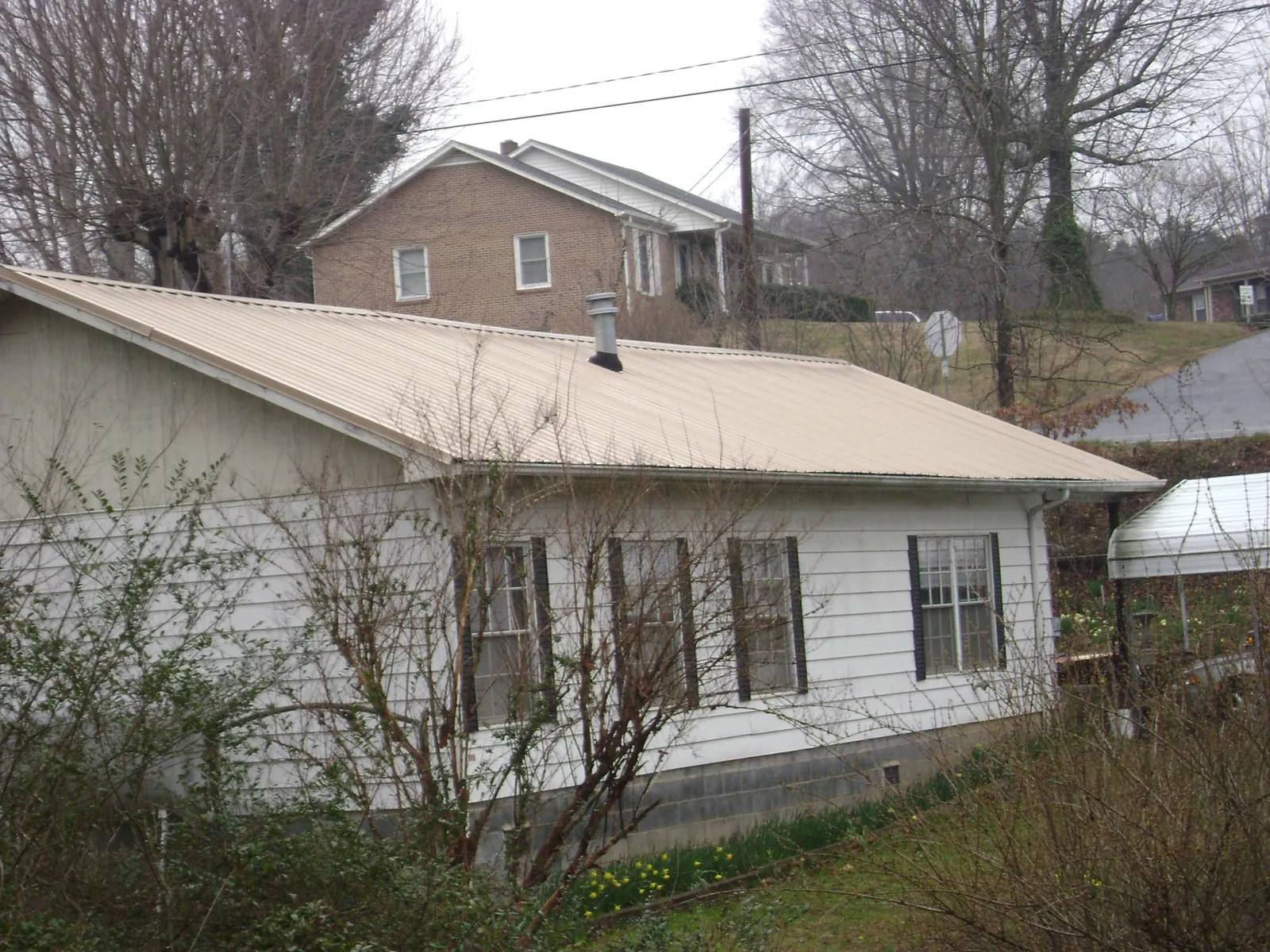 Tan metal roof on a white sided house set into a hillside — Commercial Roofing by Roofing Brothers in Wallops Island